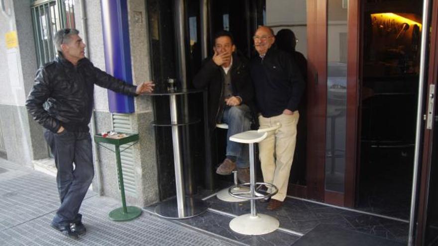 Varias personas fuman en la puerta de un bar.