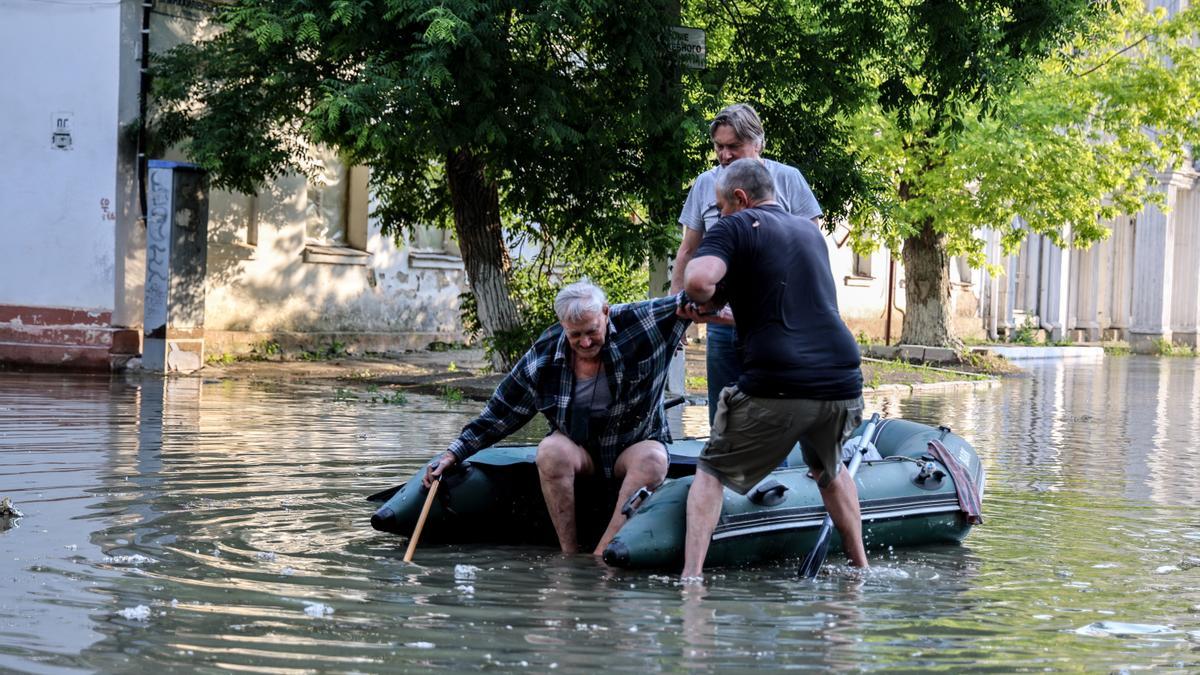 Dos personas ayudan a un hombre en una área inundada de la zona de Jersón.