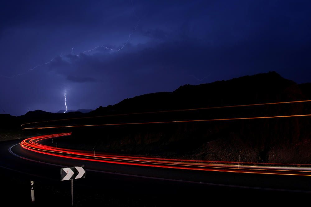 Cars drive as lightning strikes near the site ...