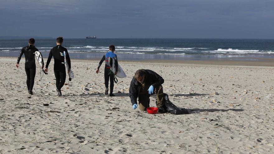 Un voluntario, observando pellets en Xagó, entre surfistas, este fin de semana pasado. | Fernando Rodríguez