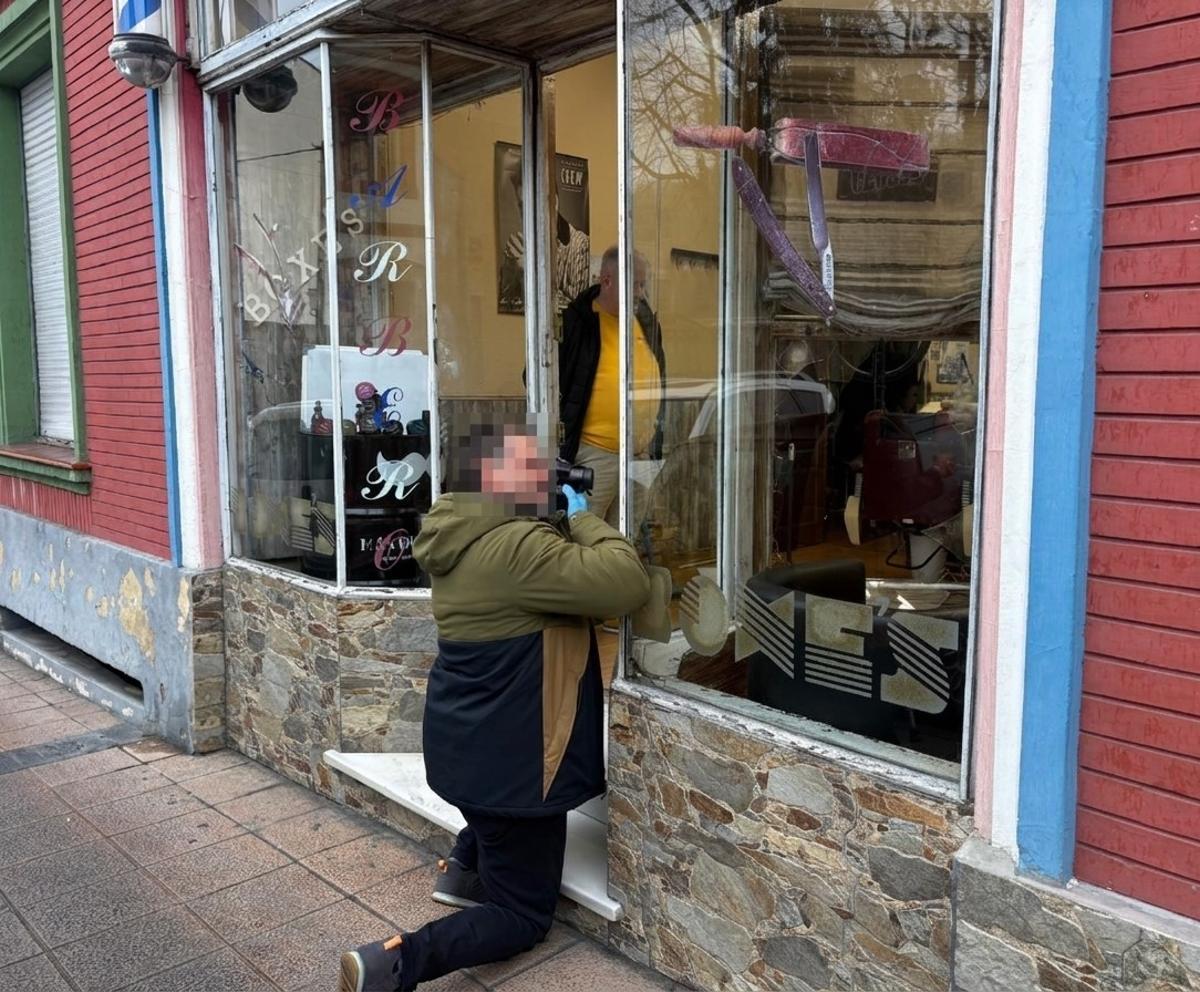 Un policía toma fotografías de las huellas en el cristal fracturado de la peluquería Boxes, en Sama de Langreo