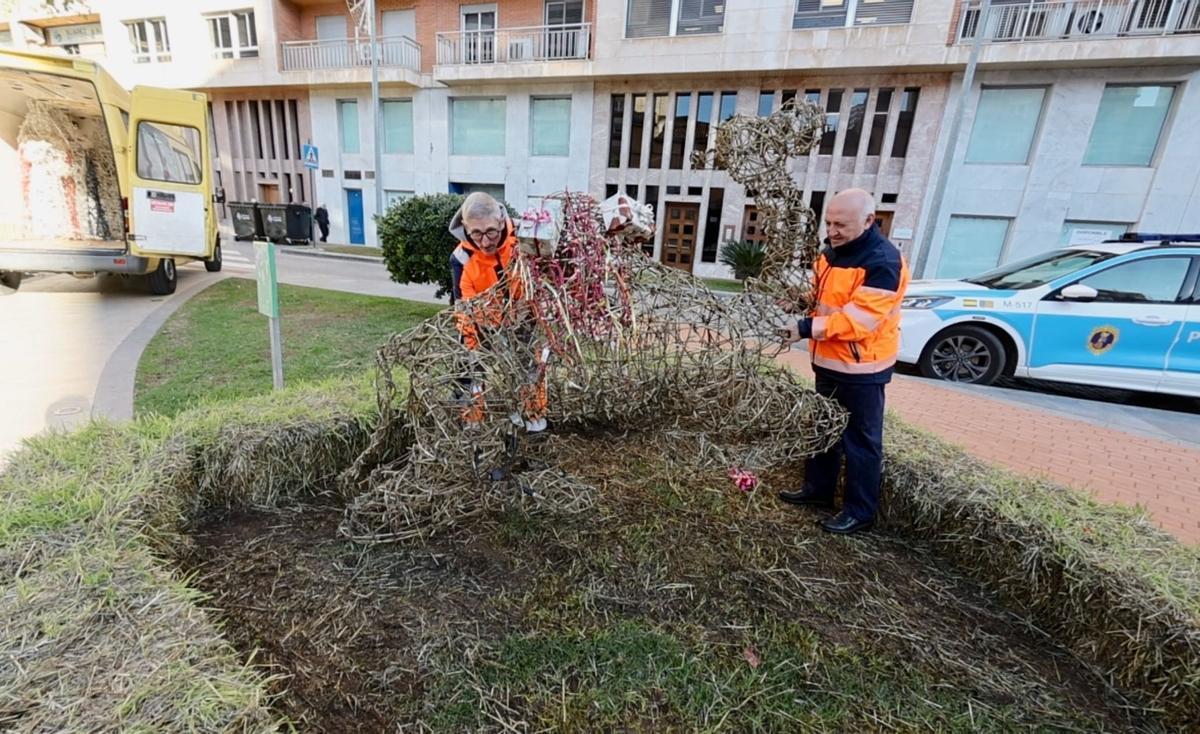 Operarios municipales retiran una figura luminosa, ya sin luces, de un camello.