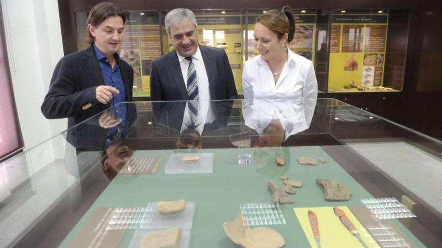 El arqueólogo que dirigió el proyecto, el alcalde y una trabajadora municipal observan la colección.