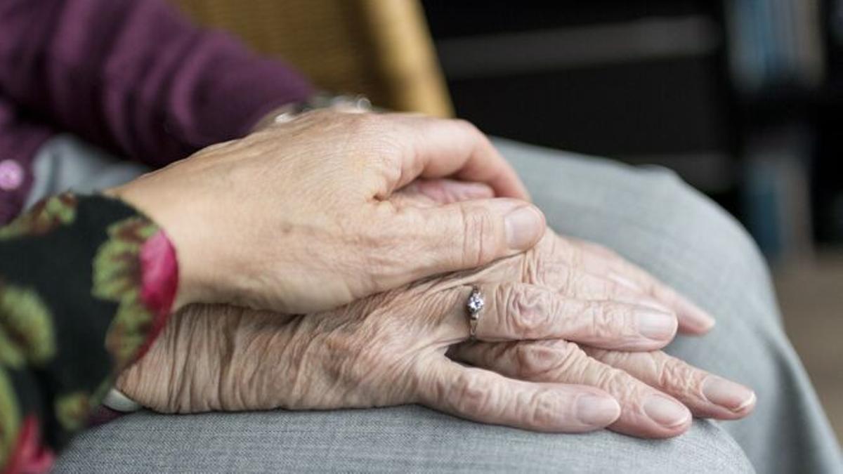 Primer pla de les mans agafades d'una cuidadora i una persona gran amb dependència.