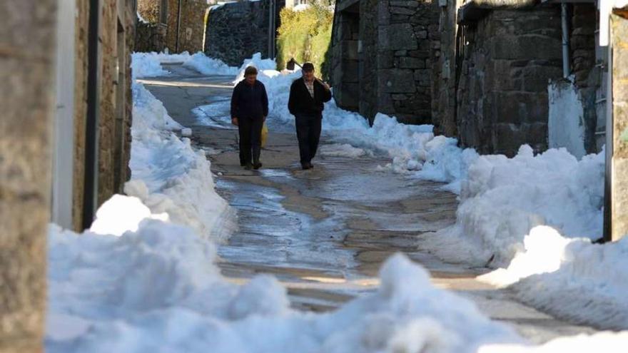 Una pareja camina entre la nieve por una calle de Villanueva de la Sierra.