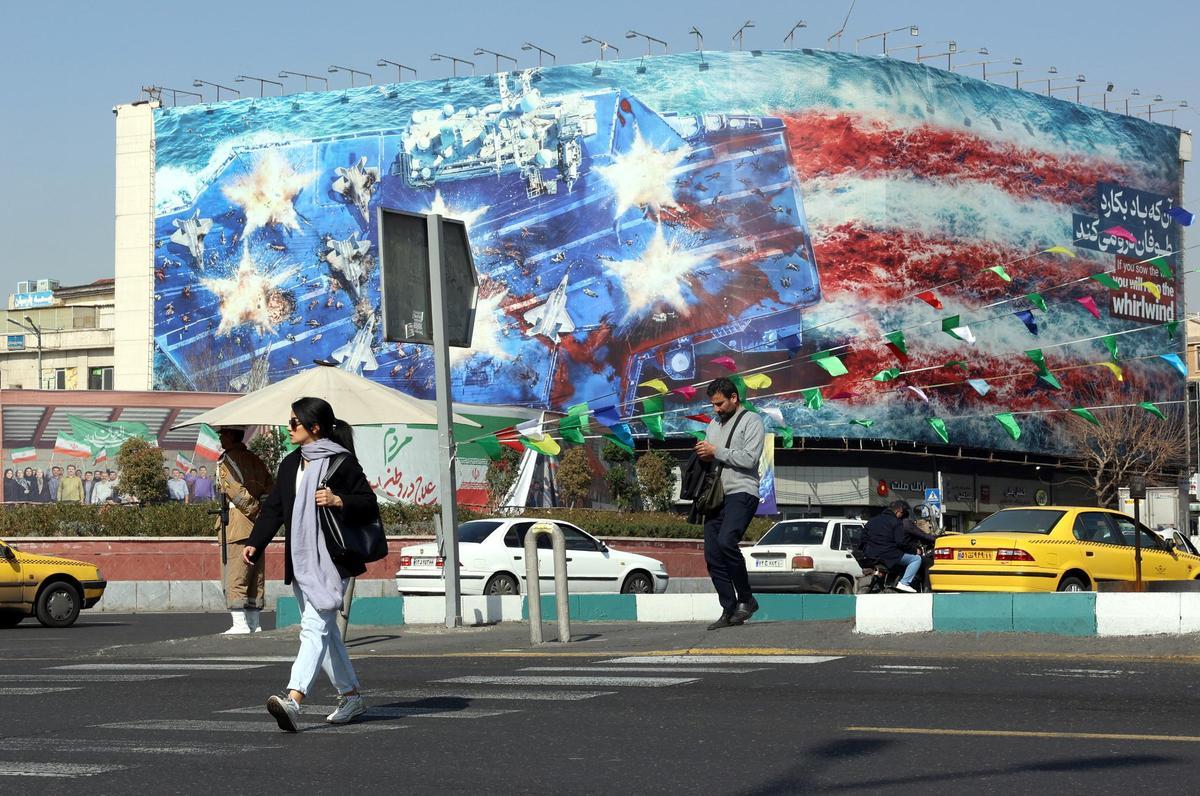 Un peatón cruza la calle cerca de una valla publicitaria antiestadounidense, en Teherán, Irán, el 19 de febrero de 2026, mientras Estados Unidos continúa aumentando su presencia militar en Oriente Medio