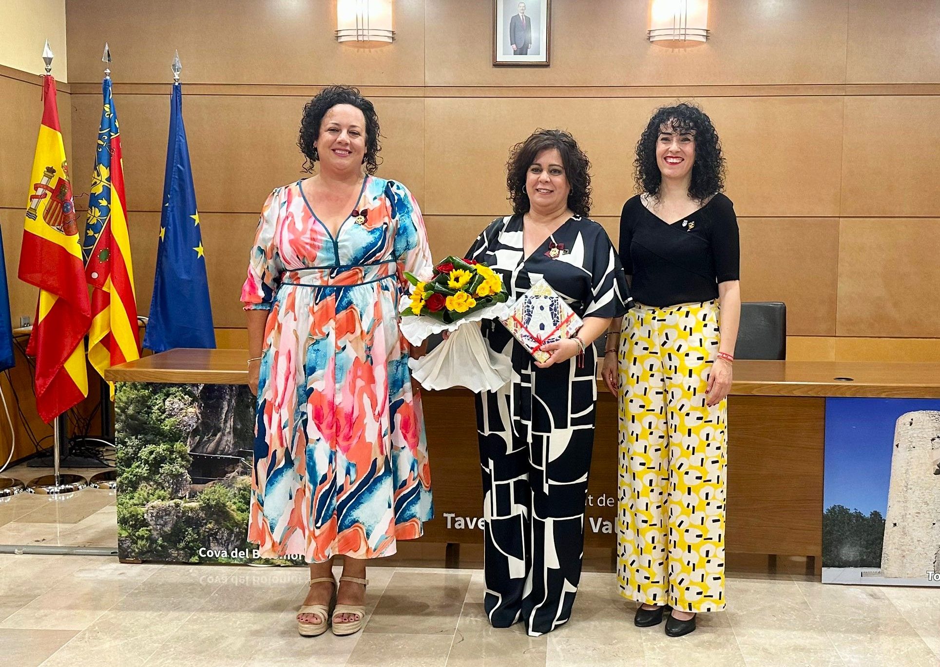 Gimeno, con ramo de flores, flanqueada por la presidenta de la FdF, a la izquierda, y la alcaldesa, a la derecha.