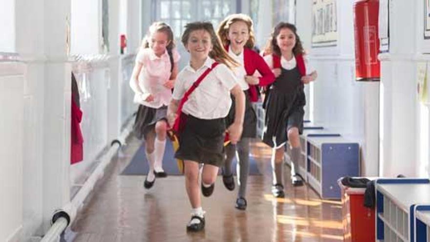 Unos niños corren con su uniforme escolar.