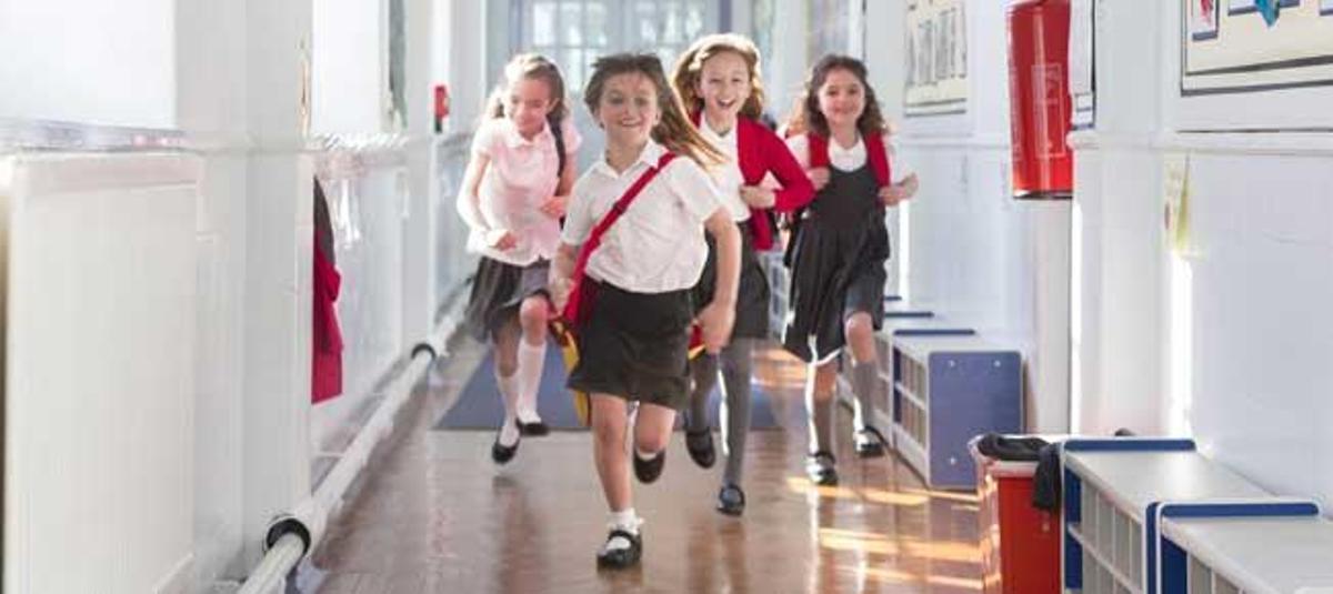 Unos niños corren con su uniforme escolar.