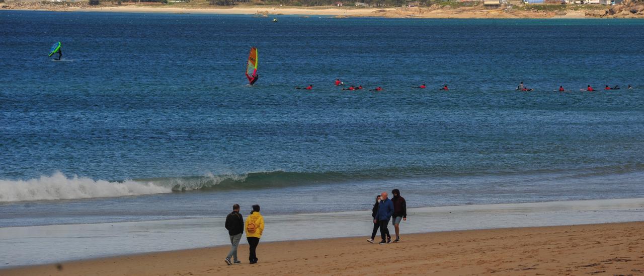 Dos tablas de surf y un buen número de surfistas observados desde la orilla por los ciudadanos que pasean por A Lanzada.