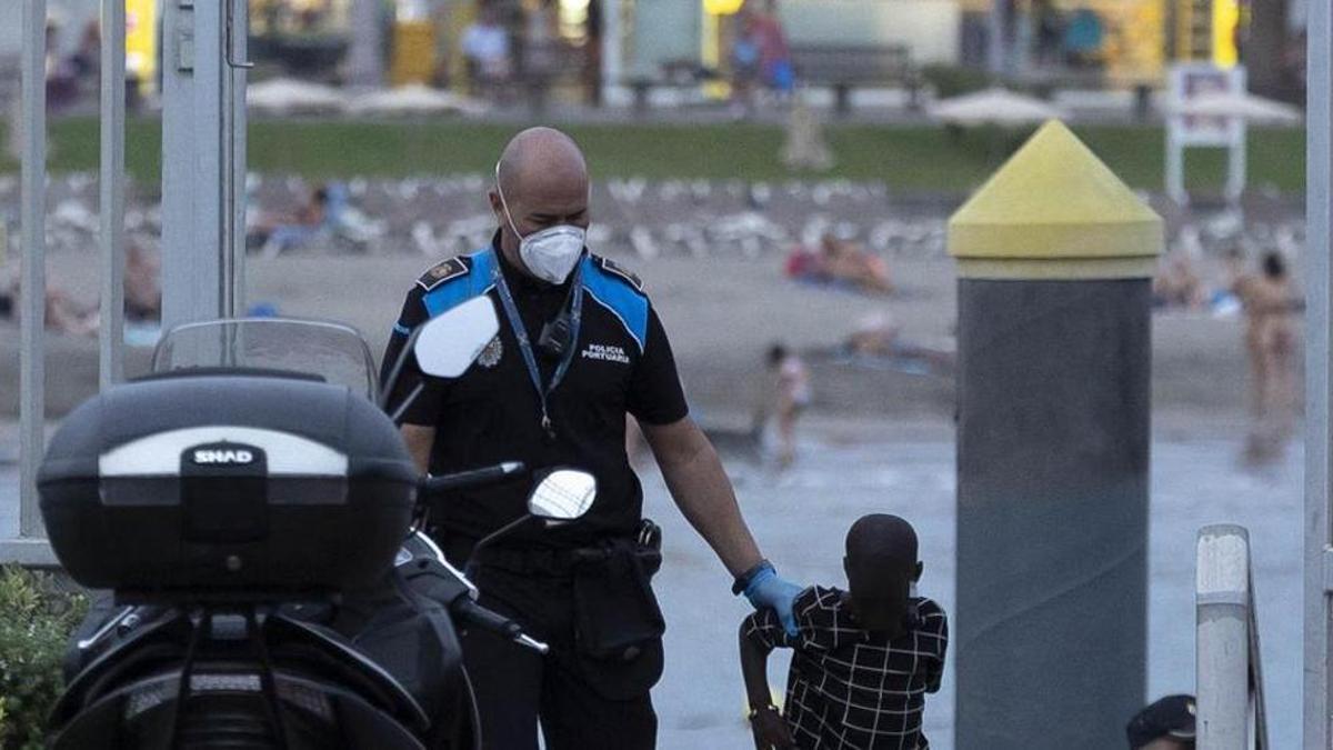 Un agente de la Policía Portuaria traslada a un menor tras desembarcar de una patera el pasado domingo en el puerto de Los Cristianos, en Tenerife.