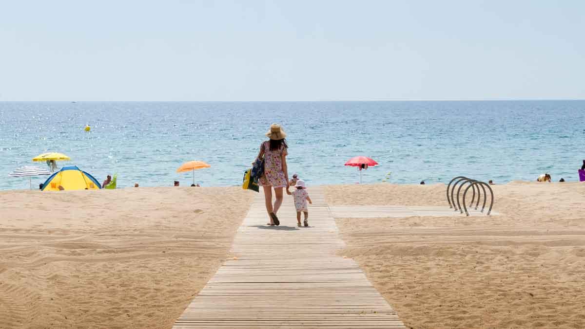 Una mujer camina junto a su hija por la pasarela de madera de la playa de Badalona.