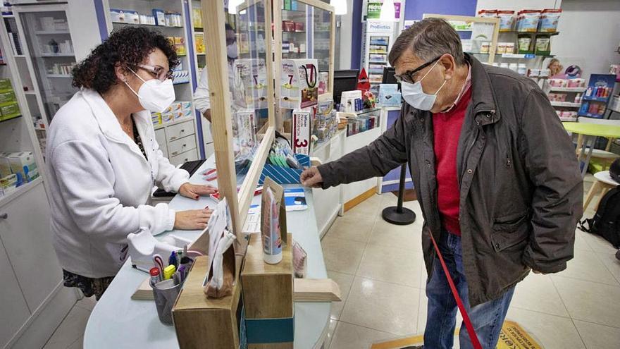 Una farmacéutica atiende a un cliente tras el cristal de protección.