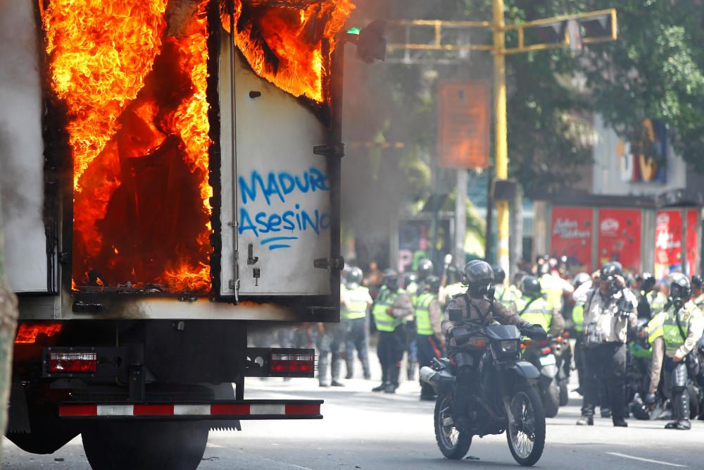Antidisturbios se reúnen junto a un camión del gobierno incendiado durante una manifestación contra el presedente venezolano, Nicolás Maduro. El graffiti dice 'asesino de Maduro'.