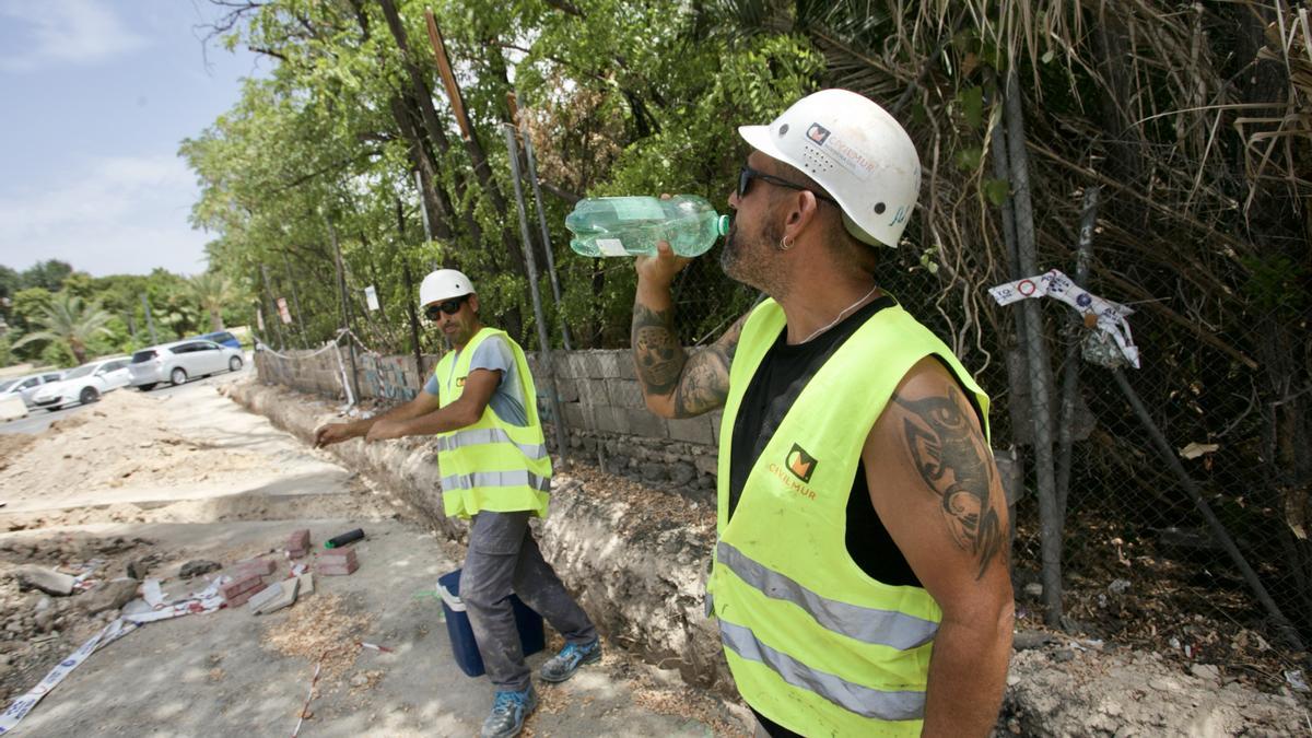 Un trabajador de la construcción bebe agua en una zona en sombra.