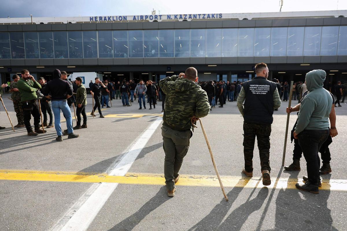 Farmers stand at Heraklion International Airport during a demonstration in Heraklion, on the island of Crete, on December 8, 2025. Farmers on Crete on Dcemeber 5 clashed with riot police near the Greek islands international airports in a burgeoning protest wave related to an EU subsidy probe. (Photo by Costas METAXAKIS / AFP)