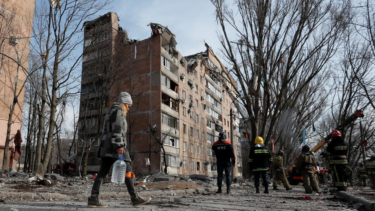 Una mujer lleva una botella de agua mientras los especialistas en emergencias trabajan en un edificio residencial dañado por los bombardeos durante el conflicto entre Ucrania y Rusia en la ciudad de Donetsk