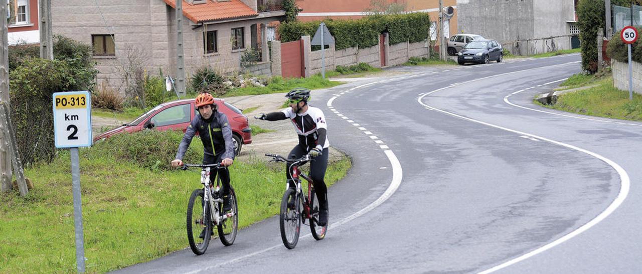 Dos ciclistas circulan por un tramo de la PO-313 donde se construirá el sendero peatonal. // Rafa Vázquez