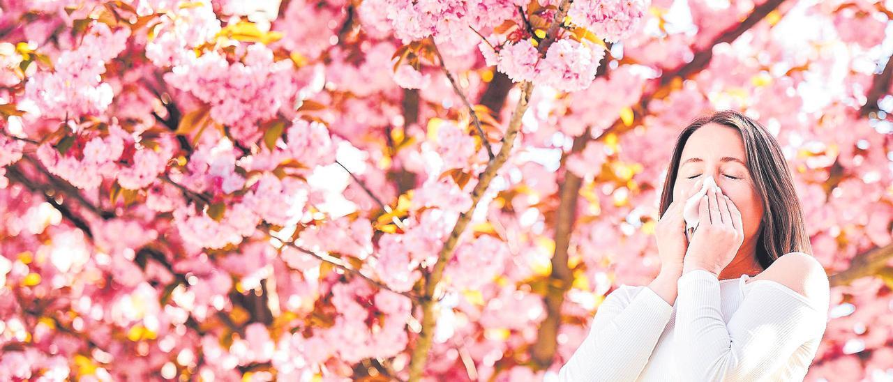 Una mujer estornuda delante de un árbol en flor.
