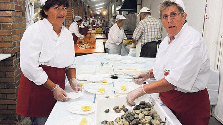 Dos mujeres preparan las raciones de almejas al natural durante la pasada edición.  //  Muñiz