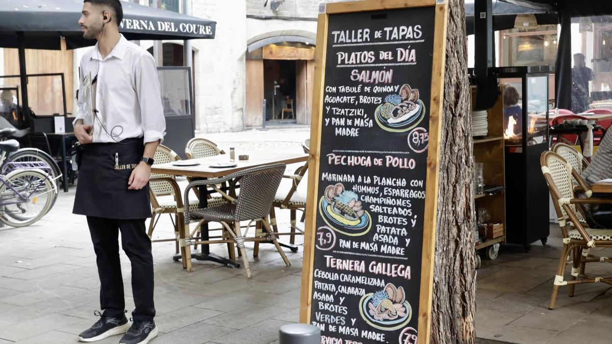 Un trabajador de un establecimiento de Barcelona espera la llegada de clientes junto a una pizarra con el menú del día.