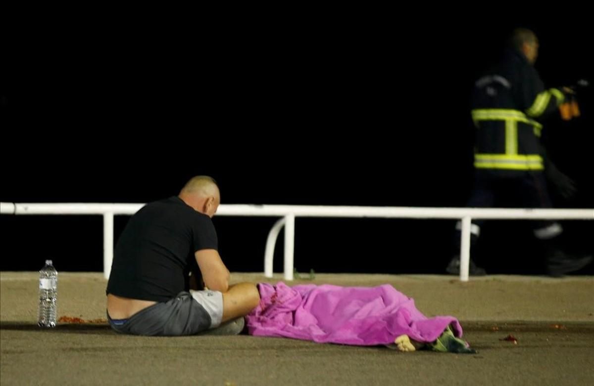 Un hombre sentado en el suelo ante un cuerpo, en el paseo de Niza.