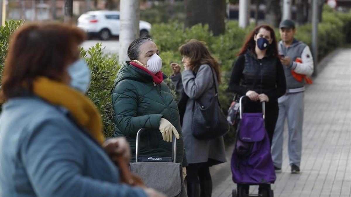 coronavirus. Clientes con mascarilla en la cola de un supermercado en el paseo de la Zona Franca