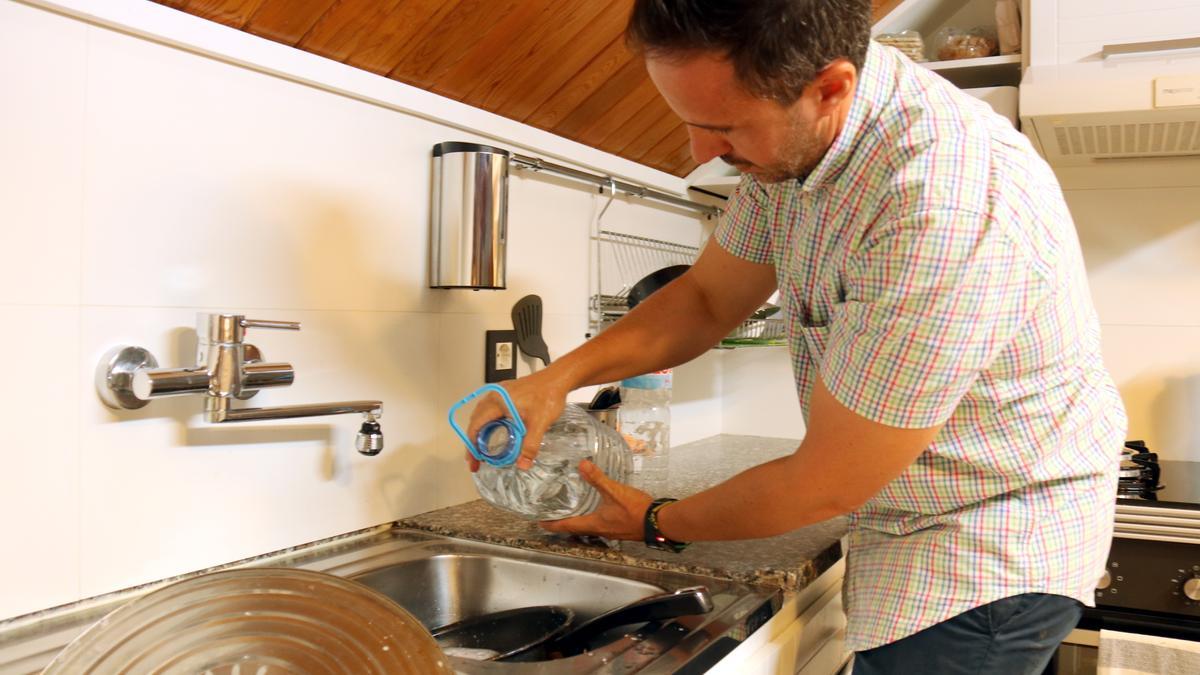 Un hombre friega una sartén con el agua de una garrafa.