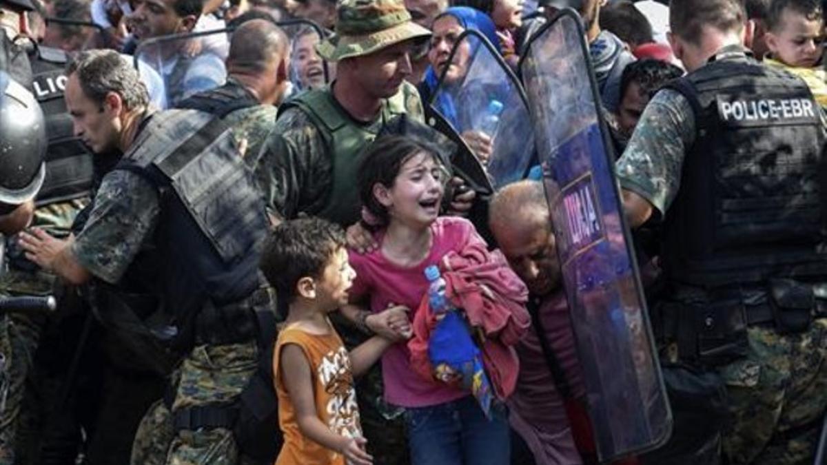 Varios refugiados ayudan ayer a uno de sus compañeros que muestra su desesperación con un niño en brazos frente a la policía de Macedonia.