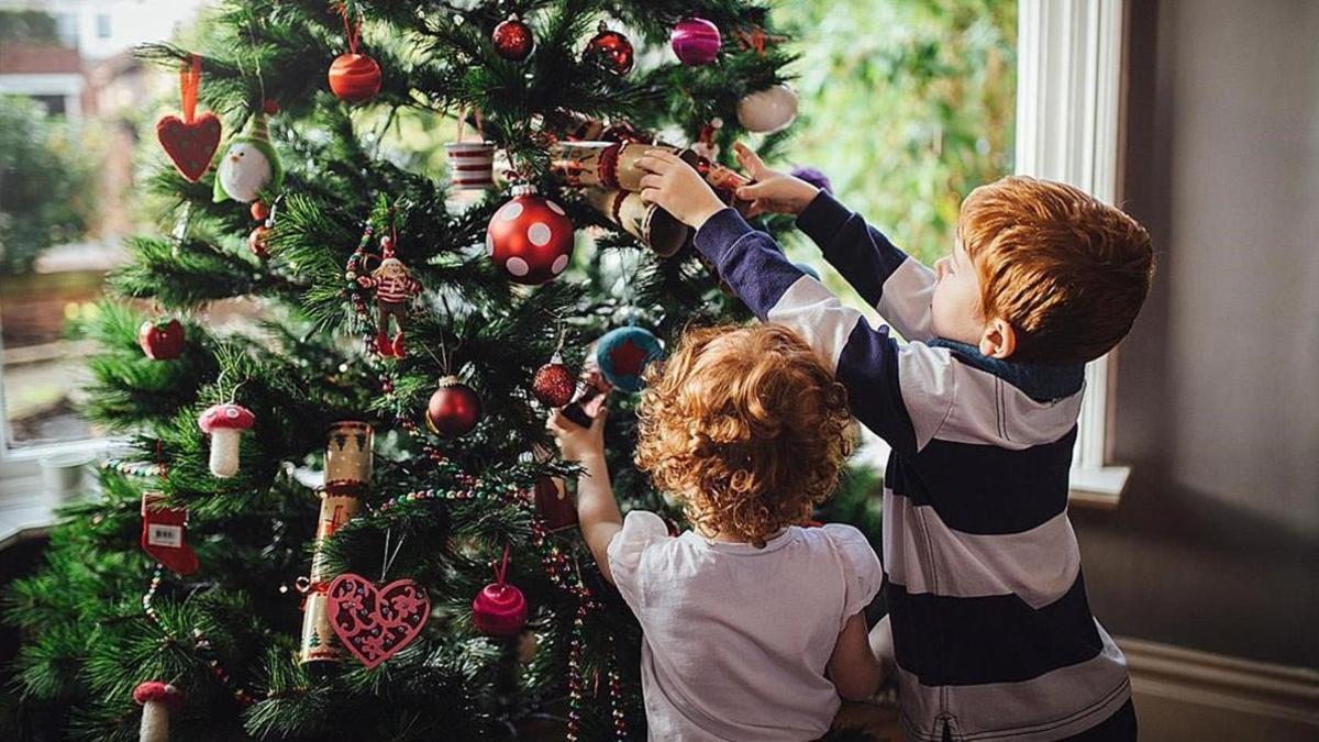 Unos niños decroran el árbol de Navidad.