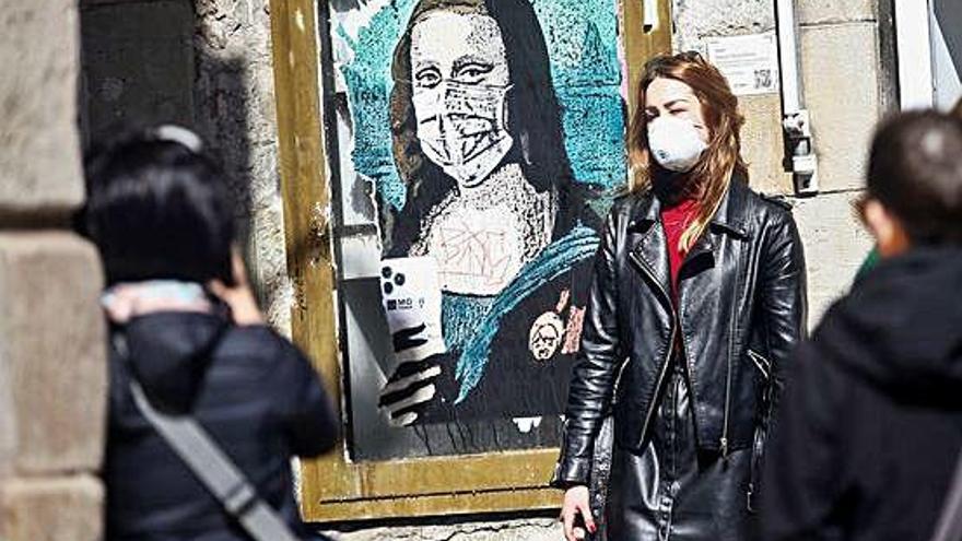 Una turista es fotografia al costat d&#039;un grafiti de la Gioconda amb mascareta, a Barcelona.