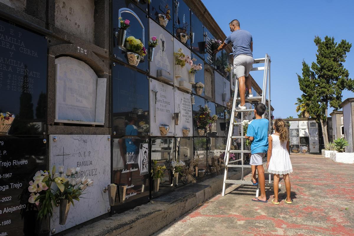Un padre subido a una escalera coloca flores en un nicho bajo la atenta mirada de sus hijos