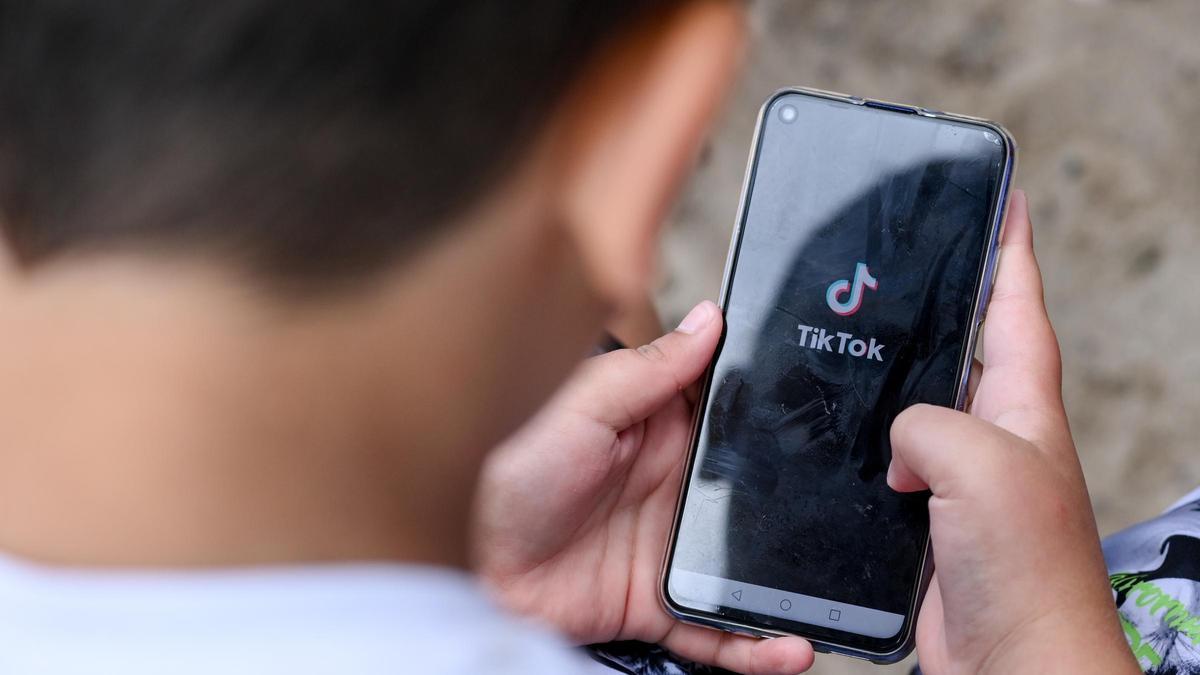 Ein Junge hält ein Smartphone in den Händen, auf dem das Logo der Kurzvideo-App TikTok zu sehen ist.