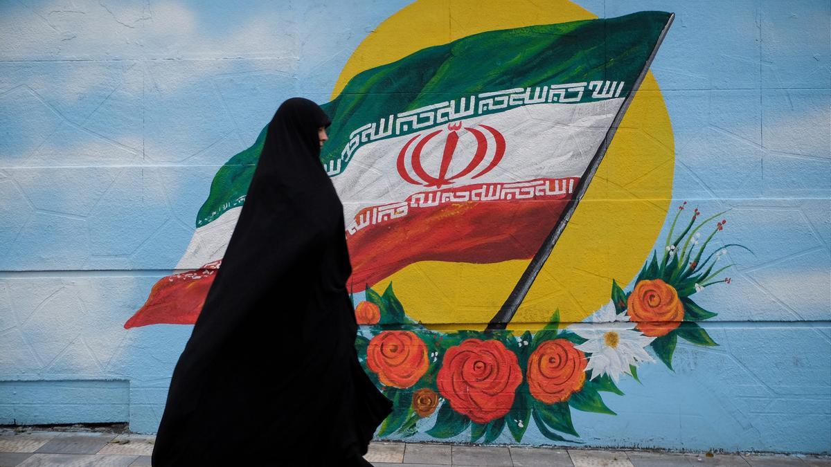 Una mujer camina junto a un mural con la bandera de Irán en Teherán.