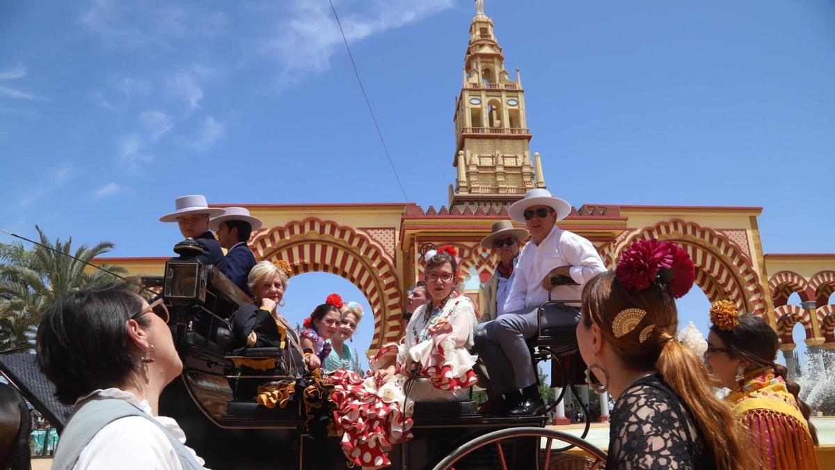 Un coche de caballos se pasea junto a la portada de la Feria de Córdoba, bajo un cielo soleado, este domingo, en El Arenal.
