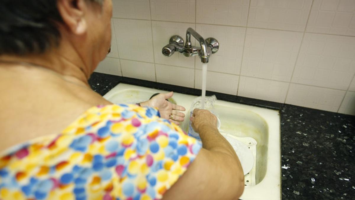 Una mujer friega los platos en la cocina de su casa.