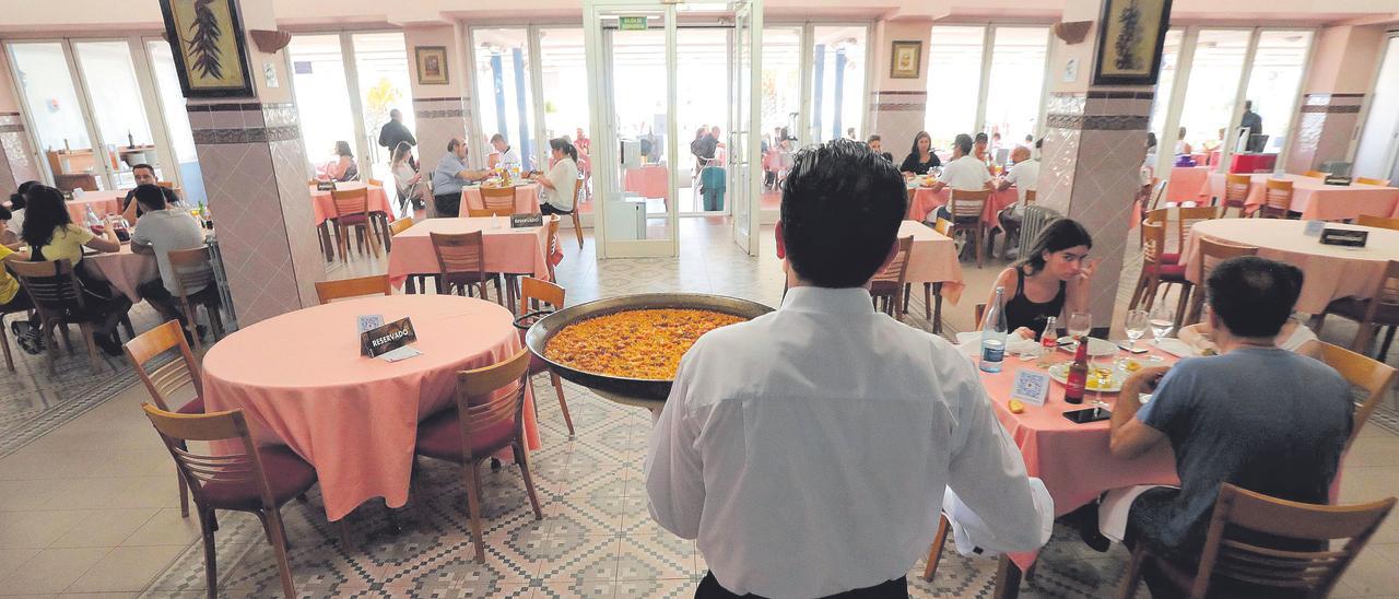 Un camarero sirve una paella a un grupo de  comensales en el comedor de un restaurante.