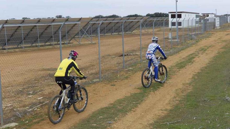 Dos ciclistas pasan junto a un parque fotovoltaico.