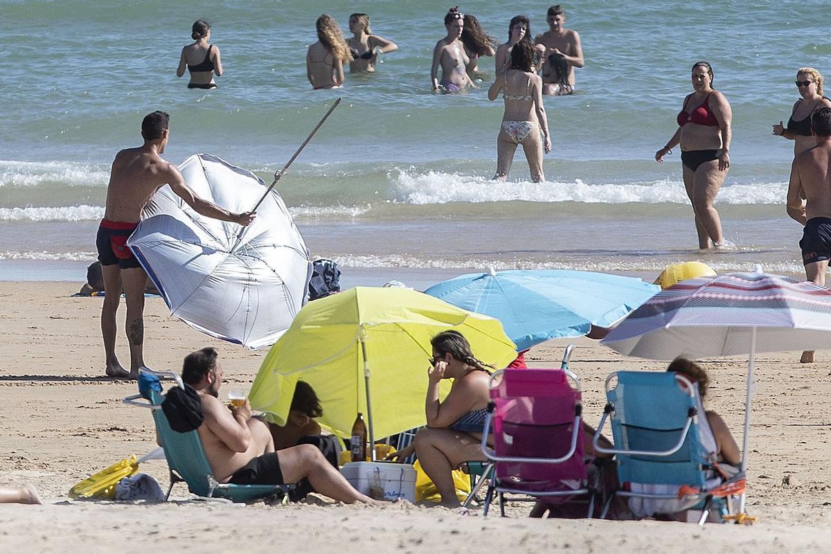 CHICLANA DE LA FRONTERA (CÁDIZ), 09/07/2022.- Un hombre recoge su sombrilla después de que saliera volando a causa del fuerte viento de levante que azota la playa de La Barrosa, en Chiclana de la Frontera (Cádiz). EFE/Román Ríos