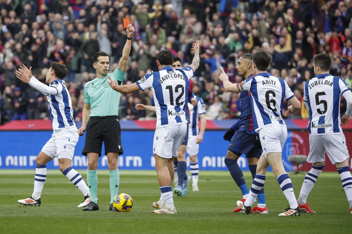 El colegiado Alejandro Quintero González (2i) muestra tarjeta roja al defensa de la Real Sociedad Aritz Elustondo (2d) durante el partido de LaLiga EA Sports entre FC Barcelona y Real Sociedad, este domingo en el estadio Olímpico de Montjuic de Barcelona. EFE/ Andreu Dalmau. (Barcelona) (real Sociedad)