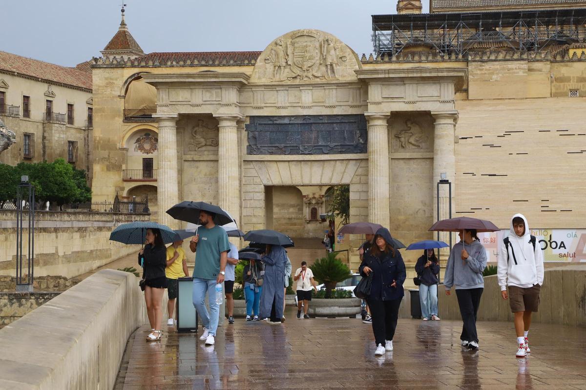 Turistas pasean bajo la lluvia en el Puente Romano.