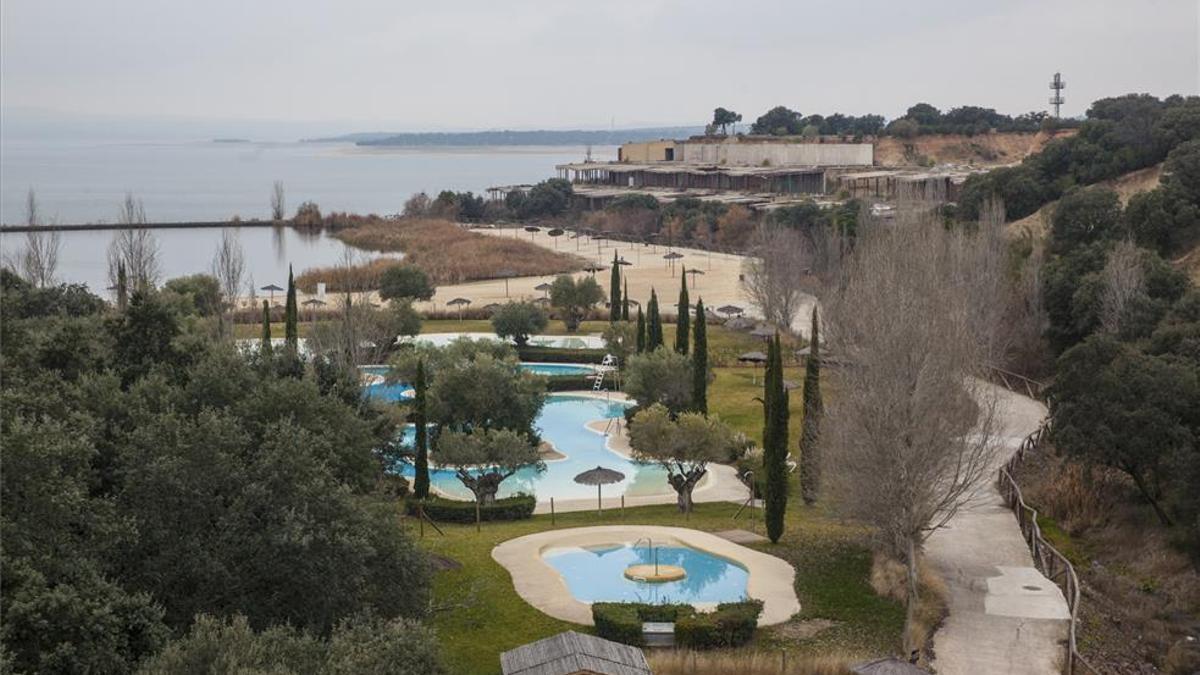 Imagen de las piscinas y playa artificial de Marina Isla Valdecañas, con edificaciones a medias al fondo.