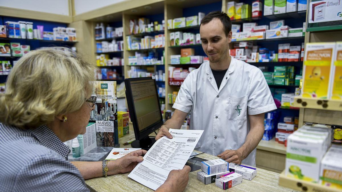 Un farmacéutico atiende a una usuaria en una oficina de farmacia.