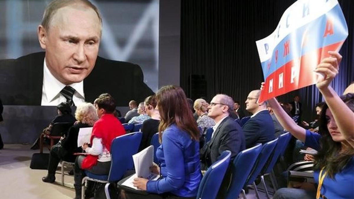 Unos periodistas agitan un cartel para llamar la atención de Vladímir Putin durante la rueda de prensa anual del presidente.