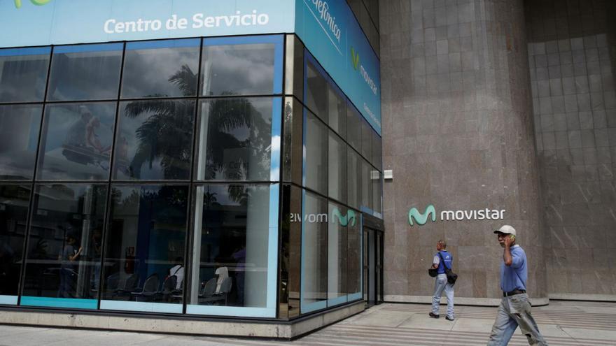 Dos transeünts passen davant unes oficines de Movistar a Caracas, en una imatge d’arxiu. | MARCO BELLO / REUTERS