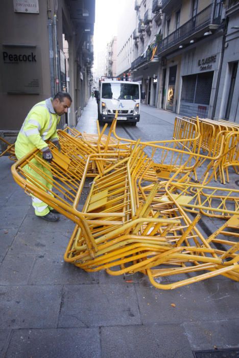 Carrers amb restes de mobiliari urbà cremat, contenidors per terra i treballadors de la brigada treballant