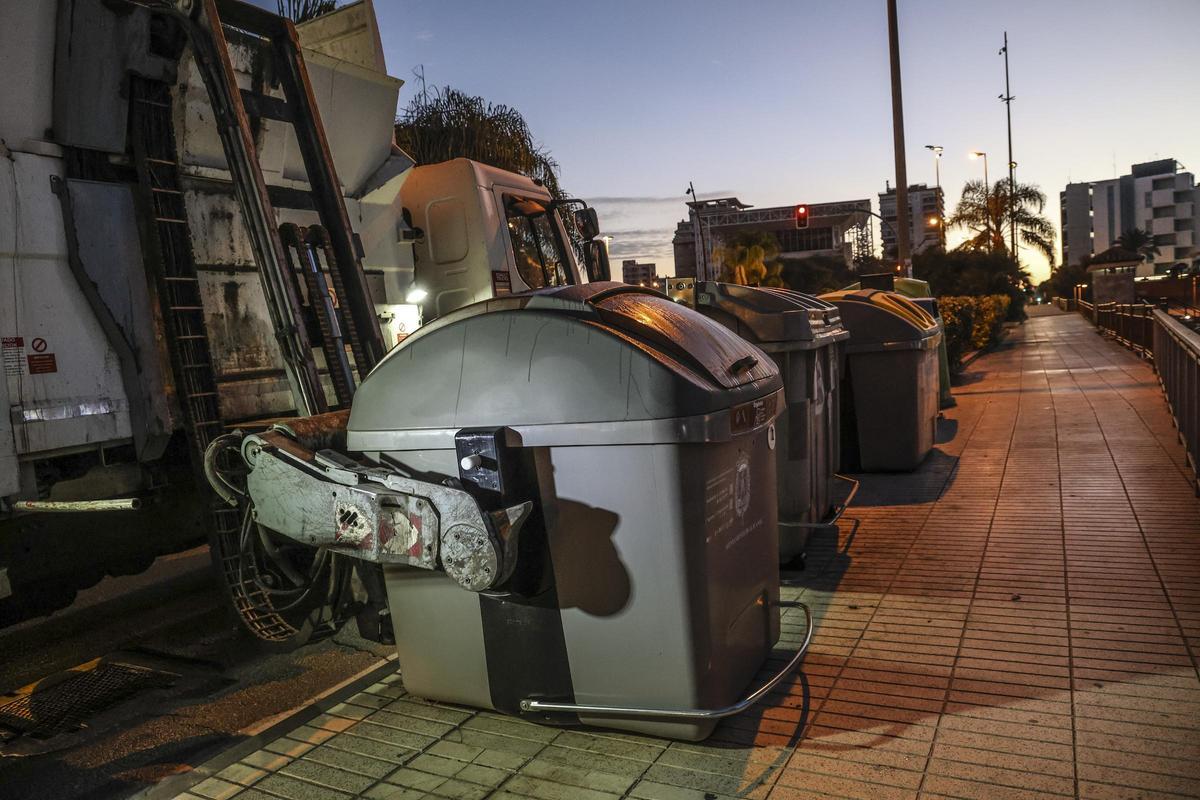 Un camión de basura recoge los contenedores al anochecer.