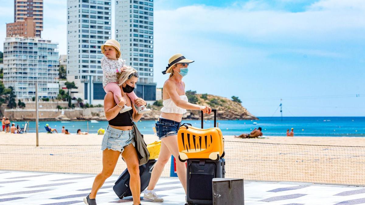 Una pareja de turistas británicas cargadas de maletas y con una niña a hombros camina por el paseo de la playa de Levante de Benidorm. | DAVID REVENGA