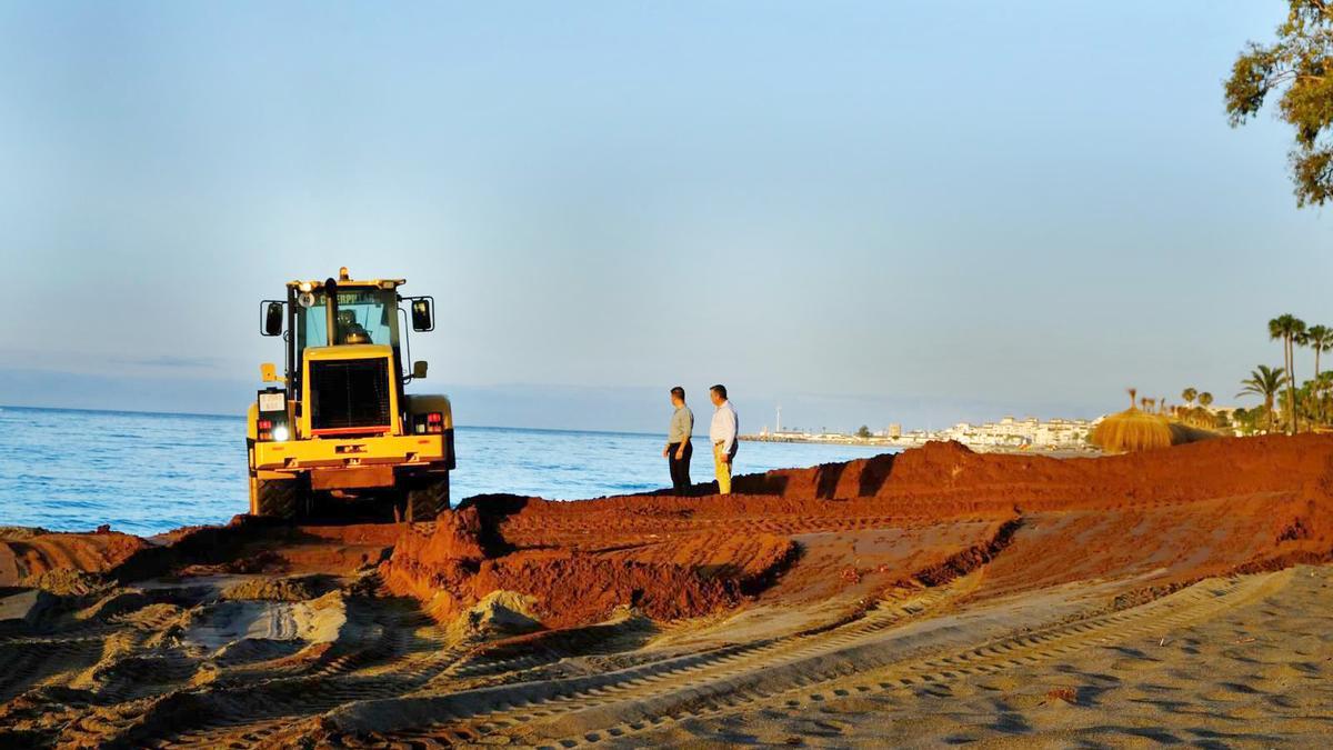 Una excavadora extiende la arena mezclada con arcilla por una playa de Marbella.