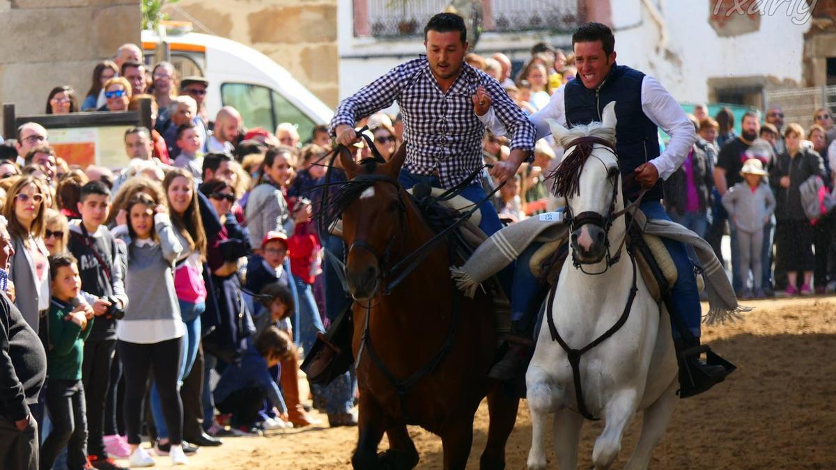 Al galope. Dos jinetes formando una collera atraviesan las calles de Navas del Madroño.